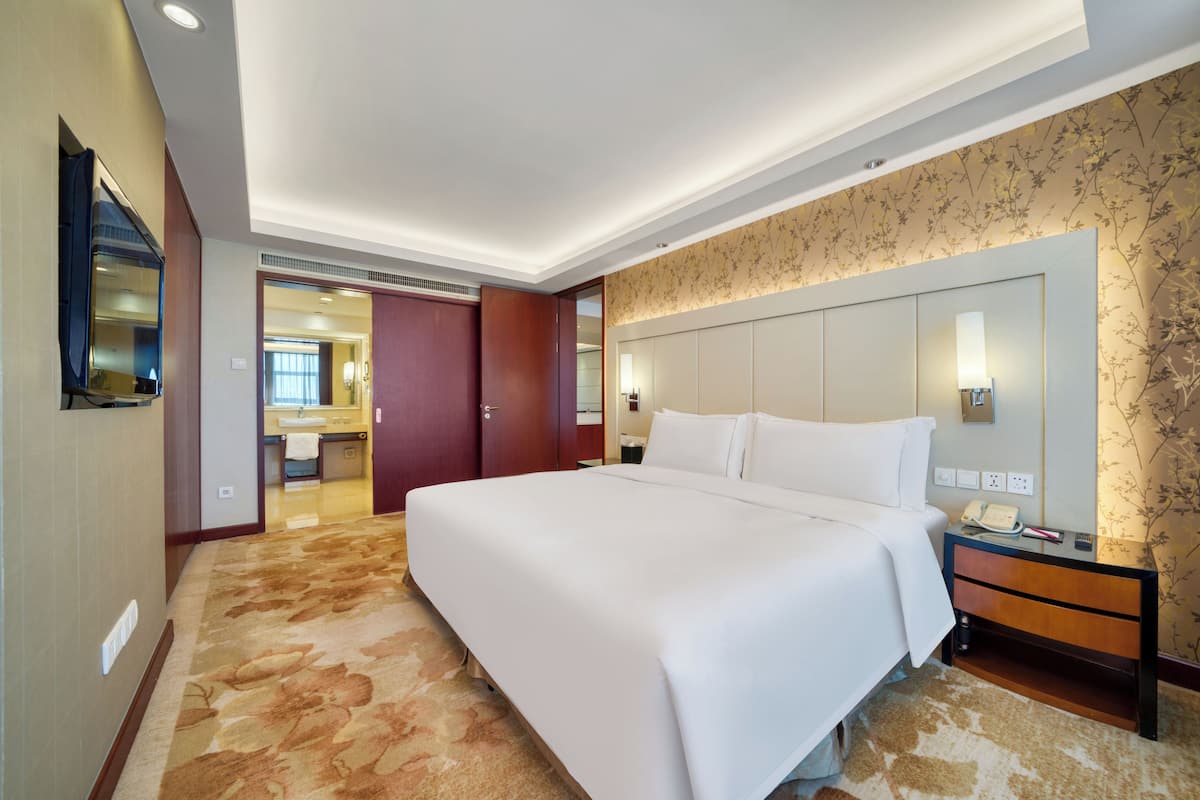 A hotel room with a large bed, a bedside table with a lamp, a mirror, and a carpeted floor.