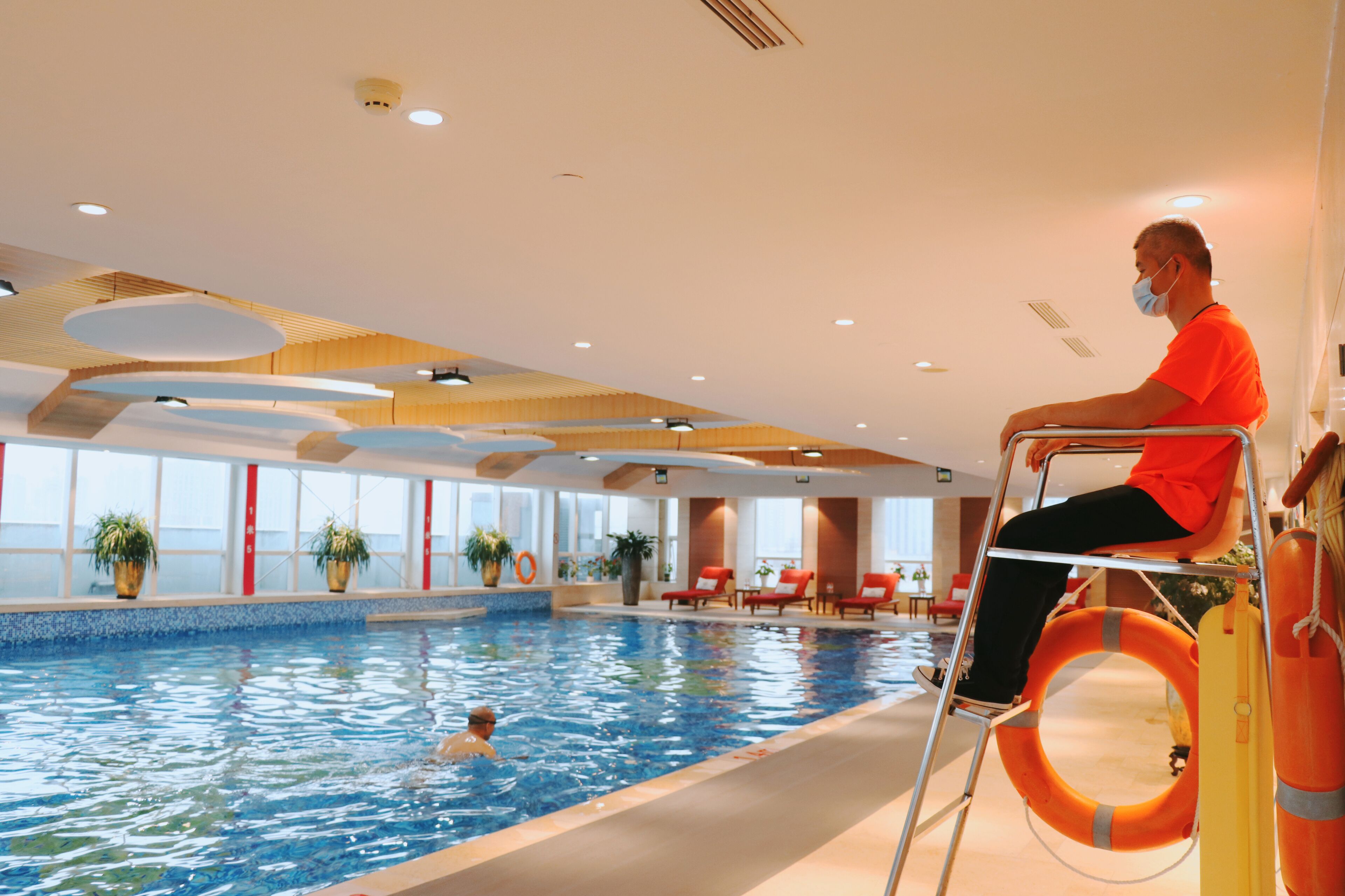 An indoor swimming pool with a person in a wheelchair and another swimming.