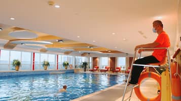 An indoor swimming pool with a person in a wheelchair and another swimming.