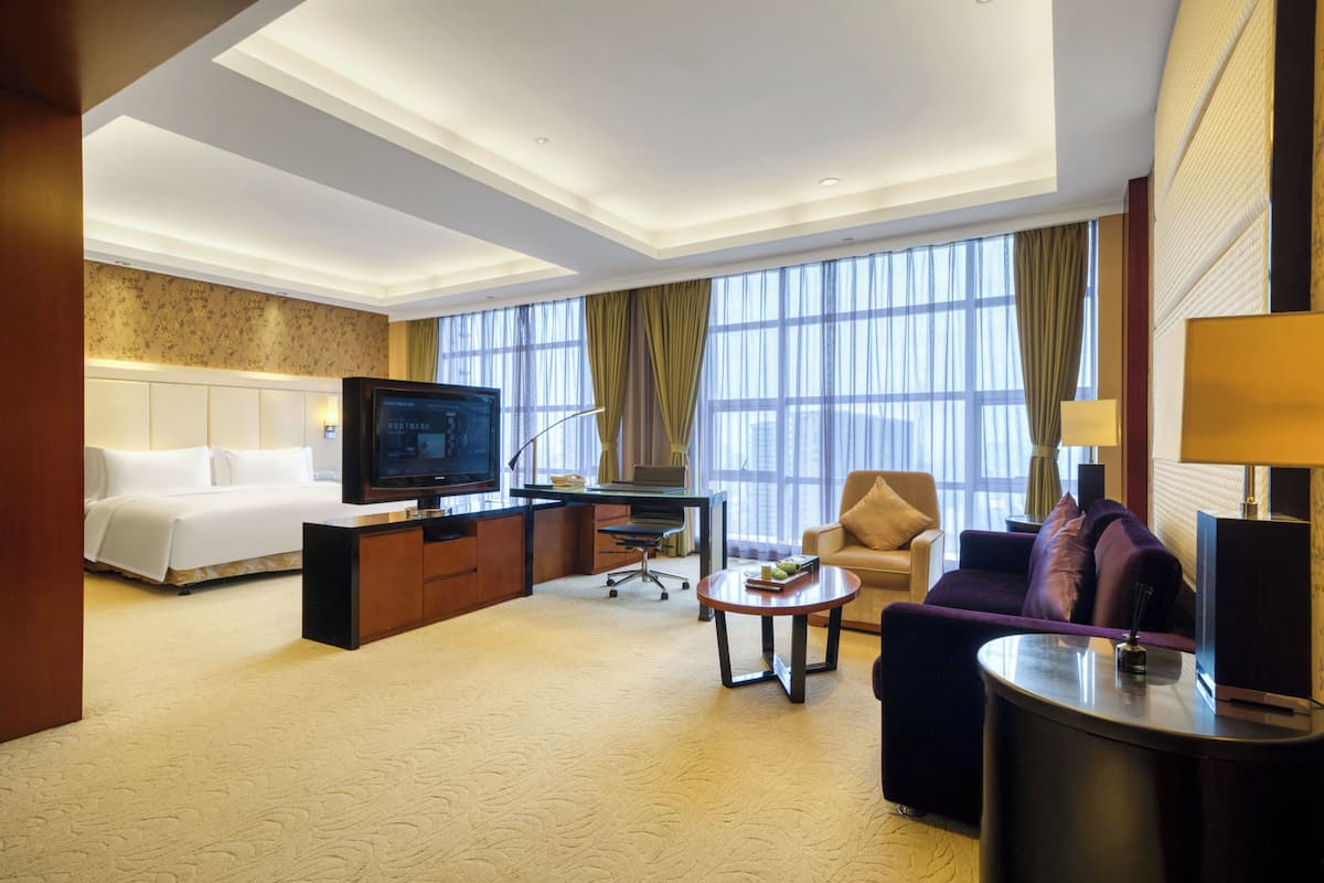 A hotel room with a bed, a desk, a television, a sofa, and a coffee table.