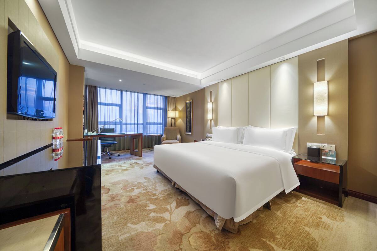 A hotel room with a large bed, a flat-screen TV mounted on the wall, a desk, and a chair.