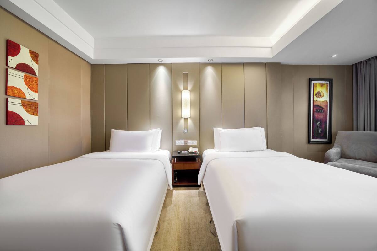 A hotel room with two beds, a nightstand, and a sofa.