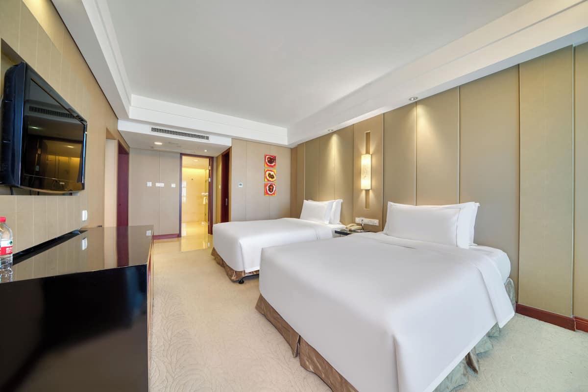 A hotel room with two beds, a flat-screen TV, a minibar, and a bathroom visible through an open door.