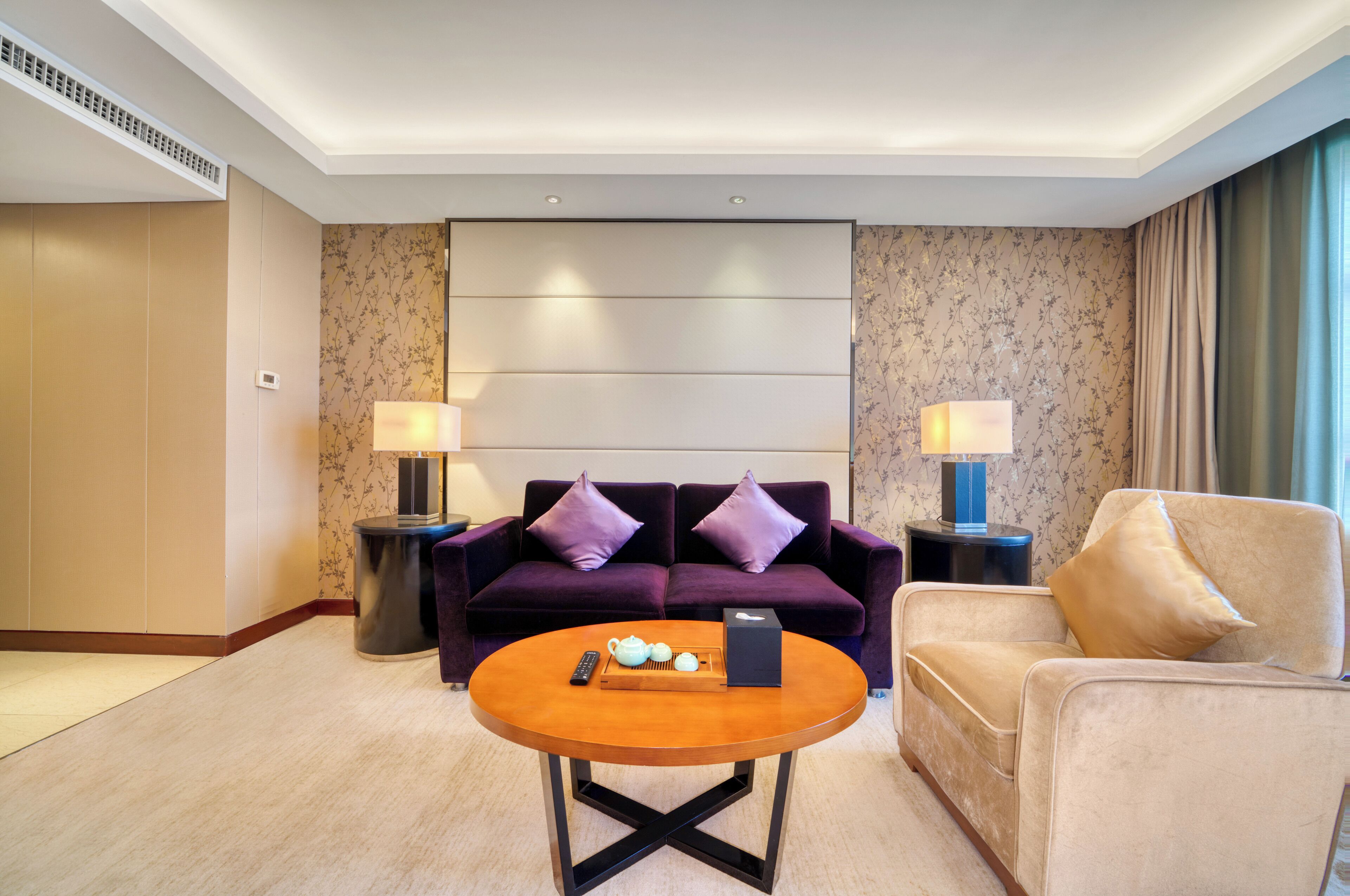 Une chambre d’hôtel comprenant un canapé, un fauteuil, une table basse ronde et deux tables de chevet avec des lampes.