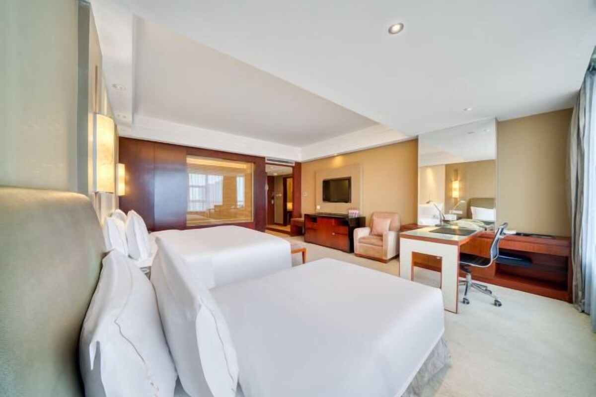 A hotel room with two beds, a desk, a chair, a TV, and a bathroom.