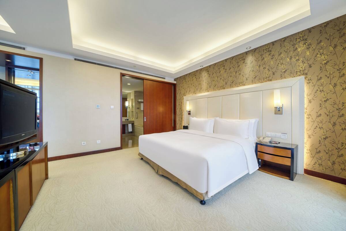 A hotel room with a large bed, a TV, a bedside table, and a wardrobe.