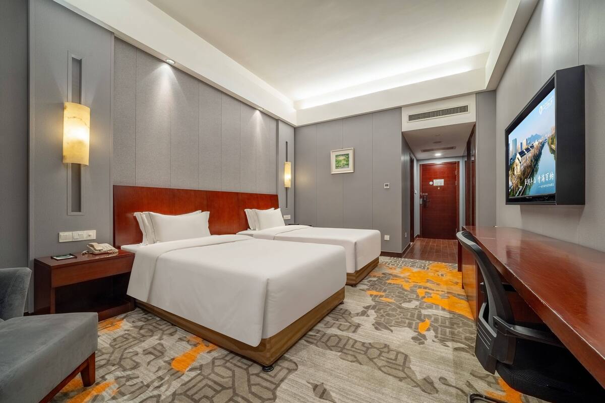 A hotel room with two beds, a desk, a TV, and a carpeted floor.