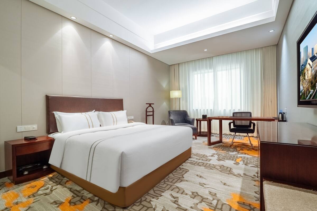 A hotel room with a large bed, a desk, a chair, and a TV.