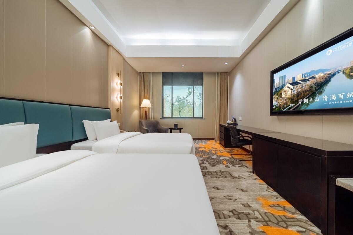 A hotel room with two beds, a desk, a TV, and a window.