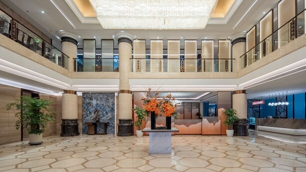 A spacious lobby with a high ceiling, a central floral arrangement, and a reception desk. - Haiwaihai Baina Hotel (Hangzhou)