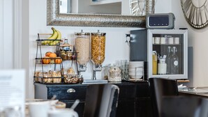 Una barra de desayuno con diversos alimentos, como plátanos y naranjas, y un refrigerador con bebidas y aderezos.
