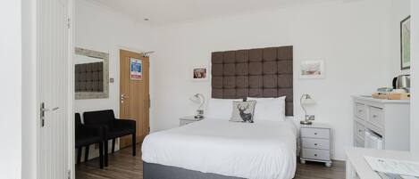 A neatly arranged bedroom with a large bed, bedside tables, a desk, and a chair.