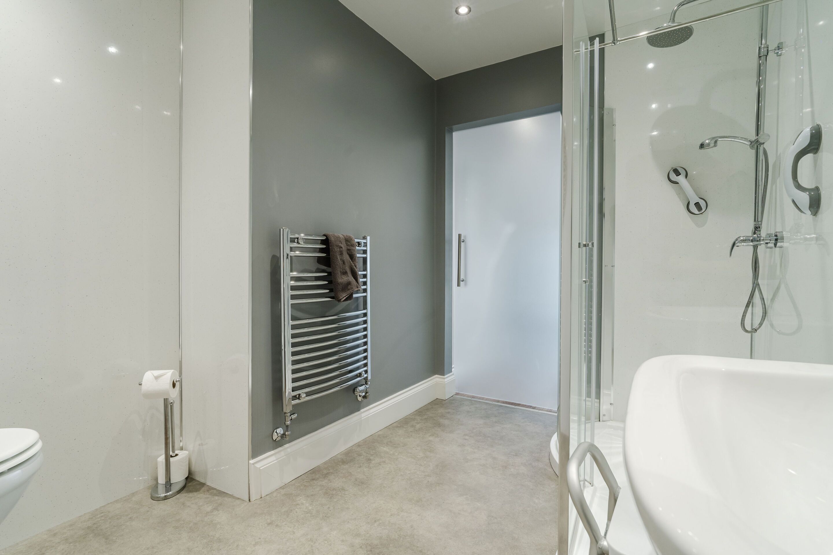 A modern bathroom with a glass shower enclosure, a white bathtub, and a towel rack with towels.