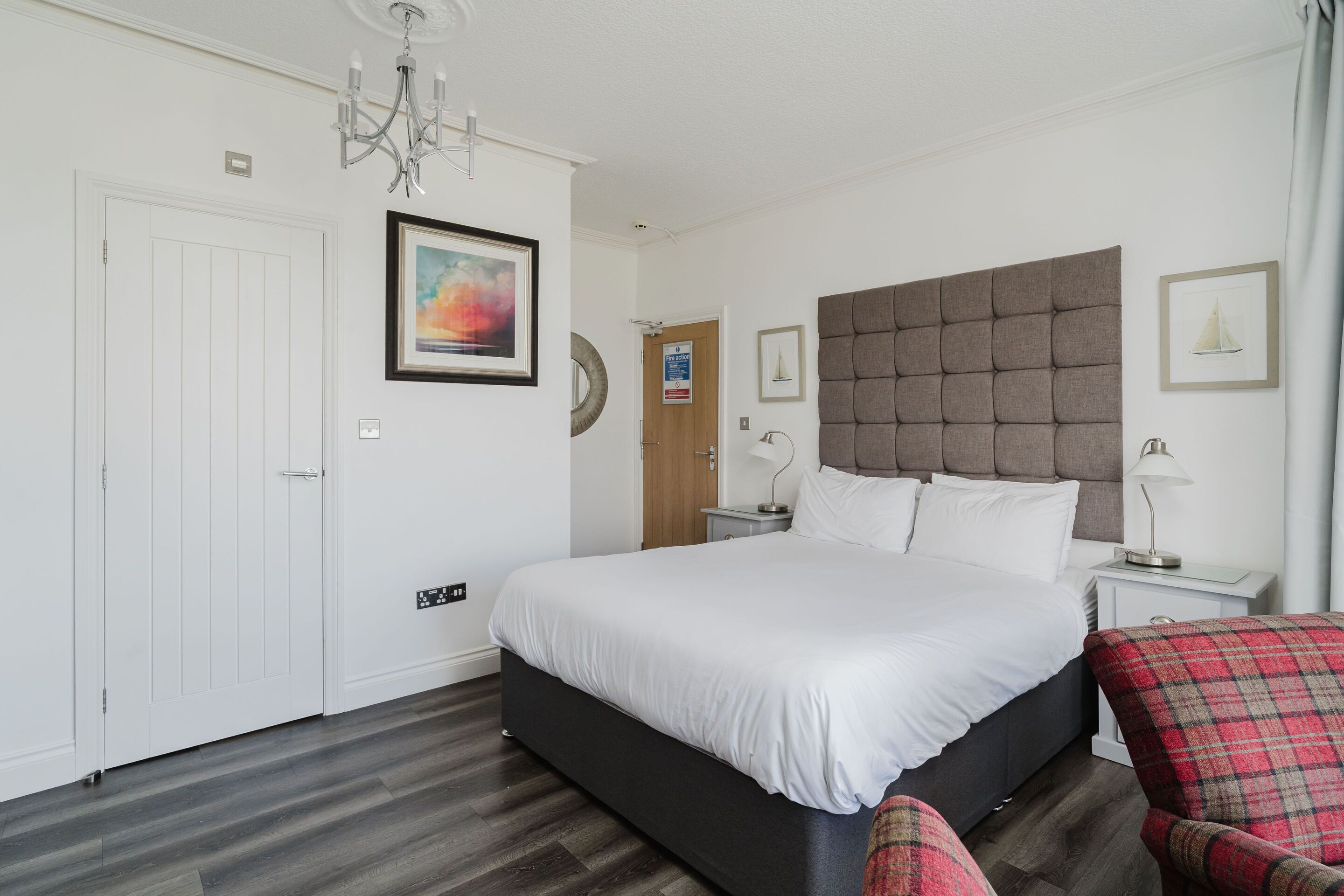 A bedroom with a large bed, a headboard, a nightstand, a chair, and a wall-mounted artwork.