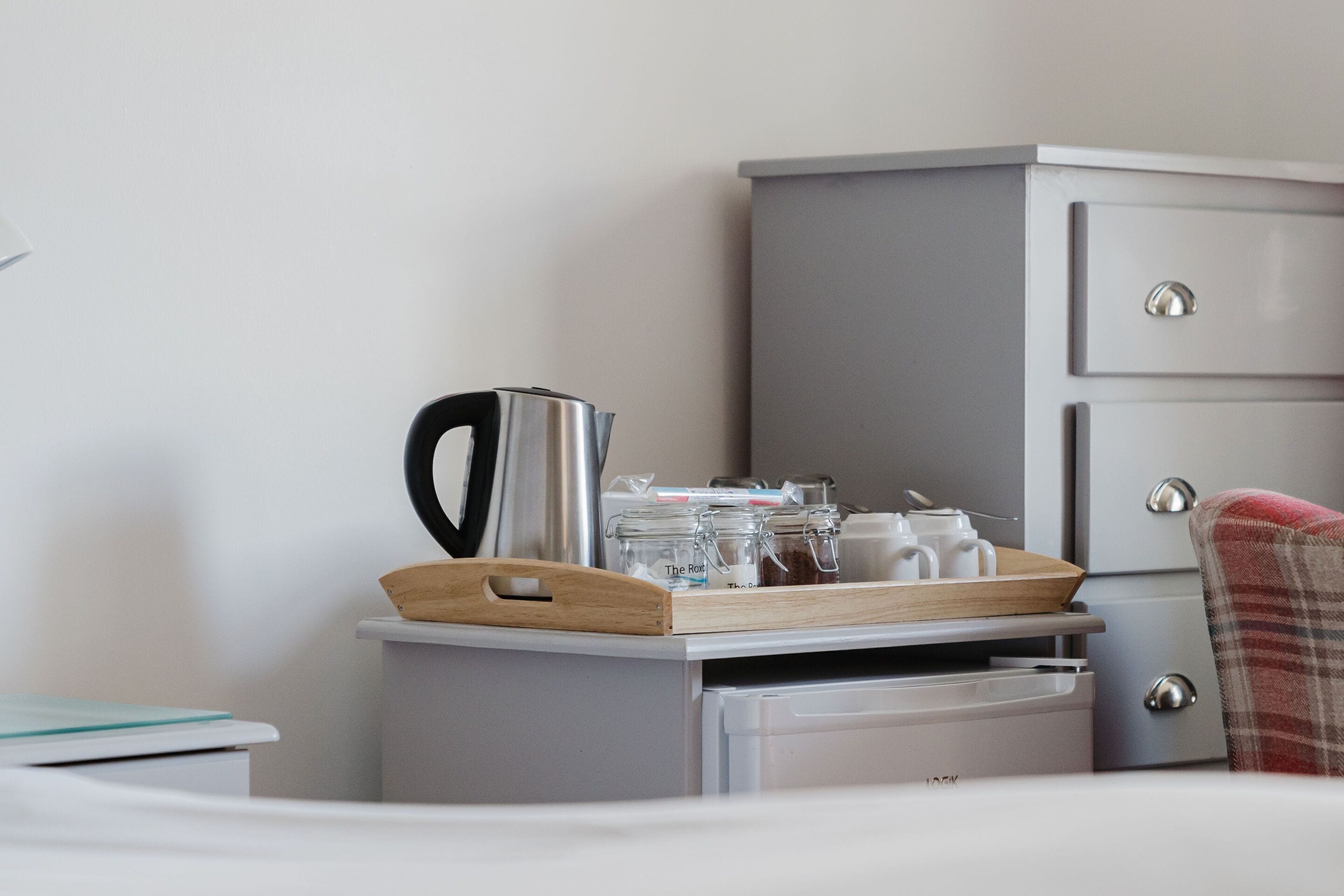 Un área de cocina ordenada con hervidor, frascos y una bandeja sobre un mueble blanco.