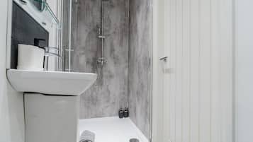 A modern bathroom with a glass shower enclosure, a white sink, and a towel on the floor.
