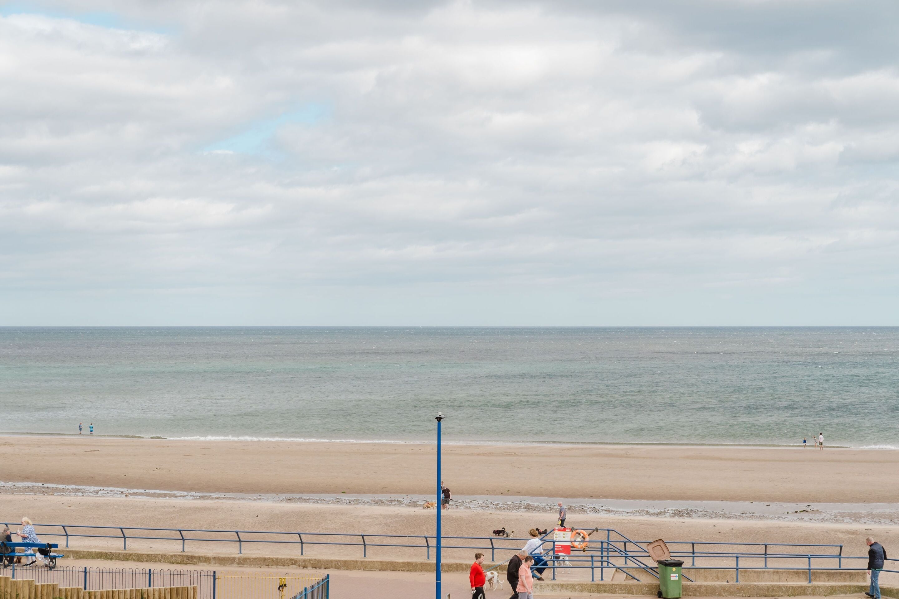 A beach with a sandy shore, a railing, and a few people.