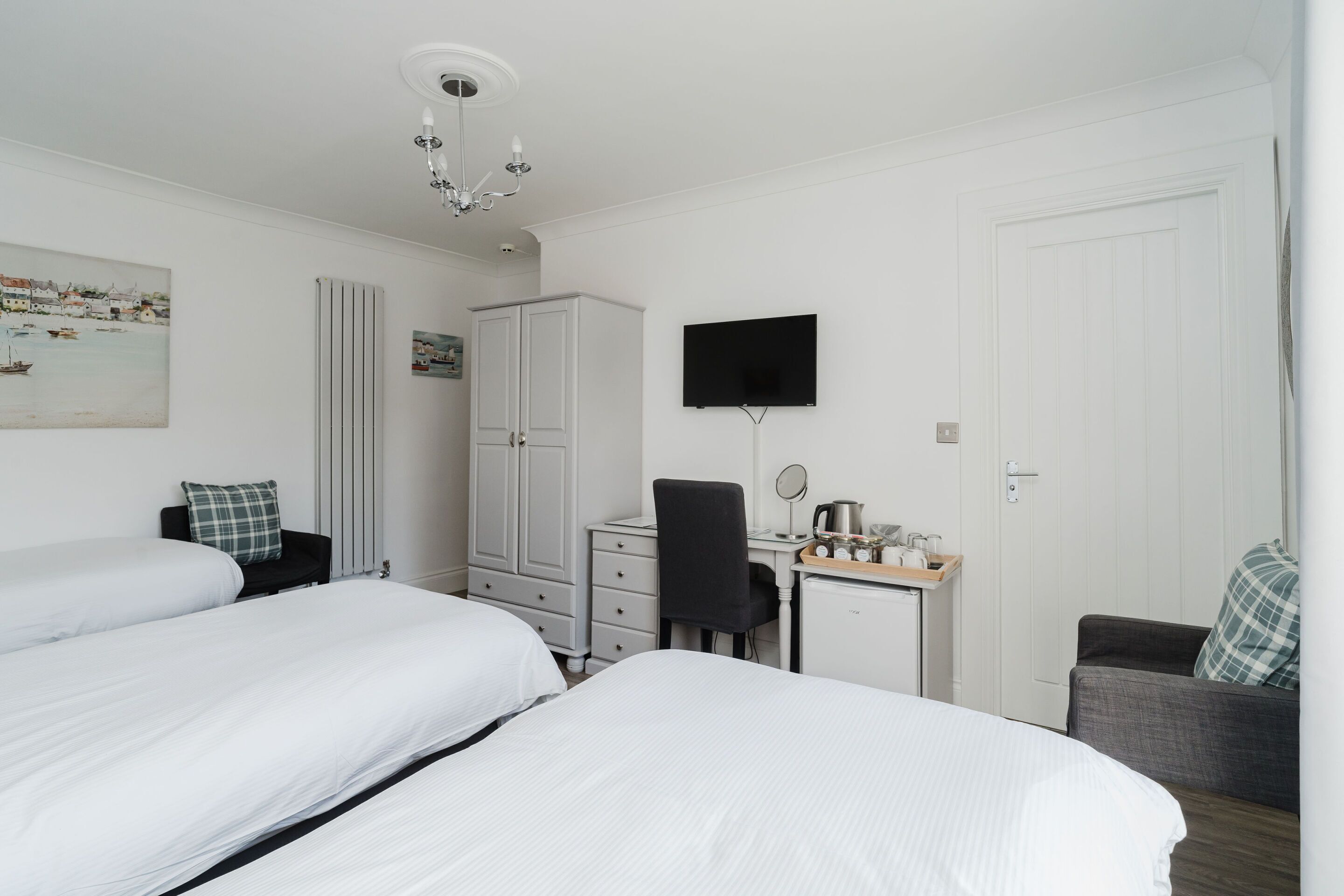 A hotel room with two beds, a desk with a chair, a television, and a wardrobe.