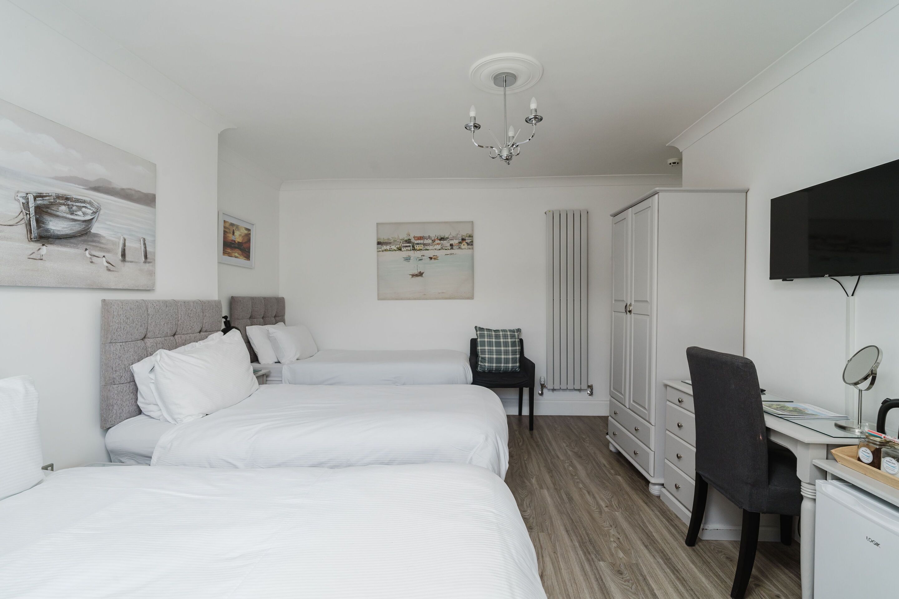 Une chambre d’hôtel avec deux lits, un bureau, une chaise, une télévision et des œuvres d’art accrochées aux murs.
