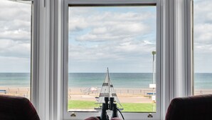 Una habitación con un amplio ventanal con vista a la playa, que incluye un telescopio y una silla.