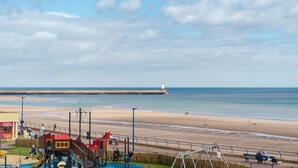 Vista de una playa con un parque infantil, un faro y una orilla arenosa.