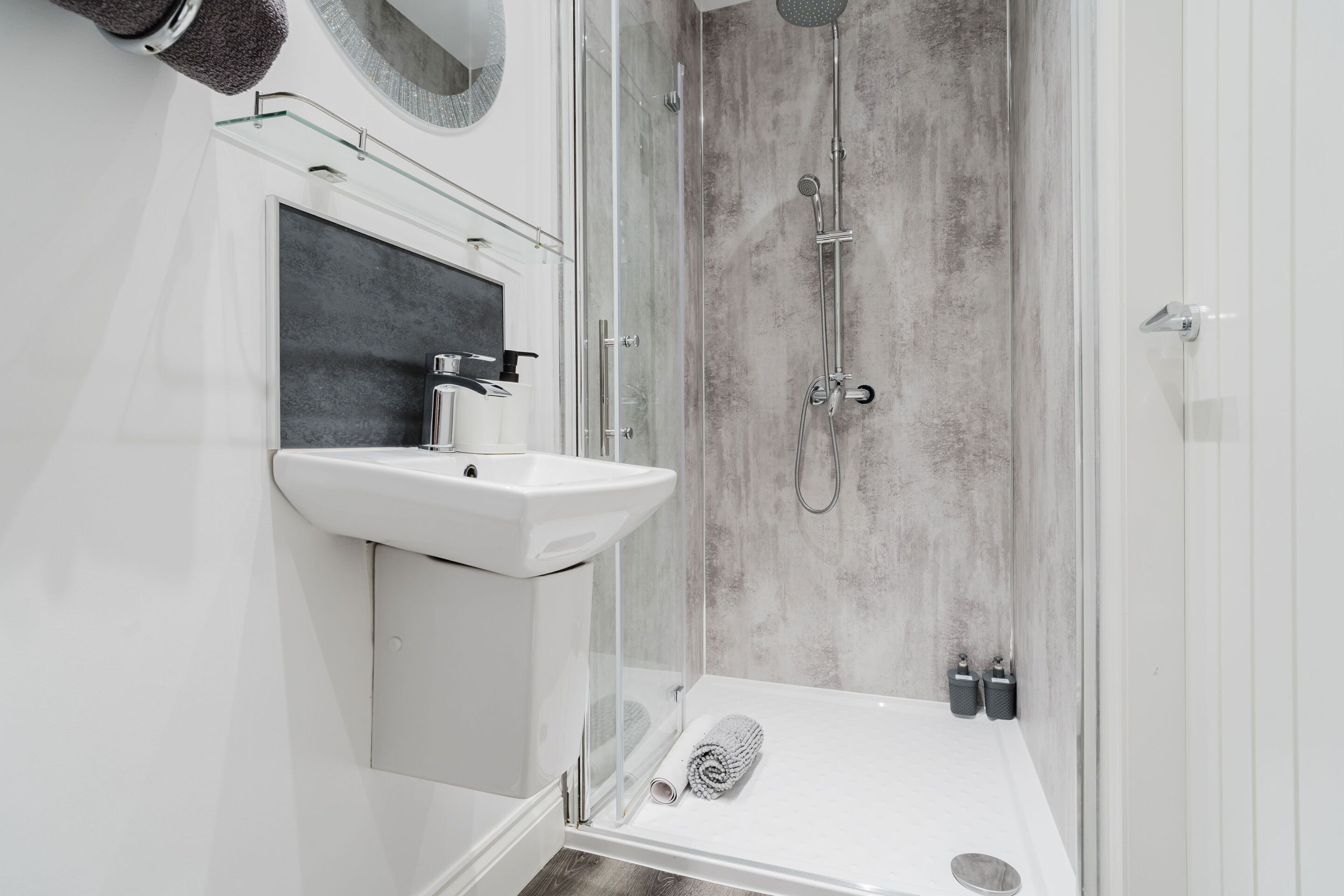 A modern bathroom with a glass shower enclosure, a white sink, and a handheld showerhead.