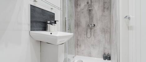 A modern bathroom with a glass shower enclosure, a white sink, and a handheld showerhead.