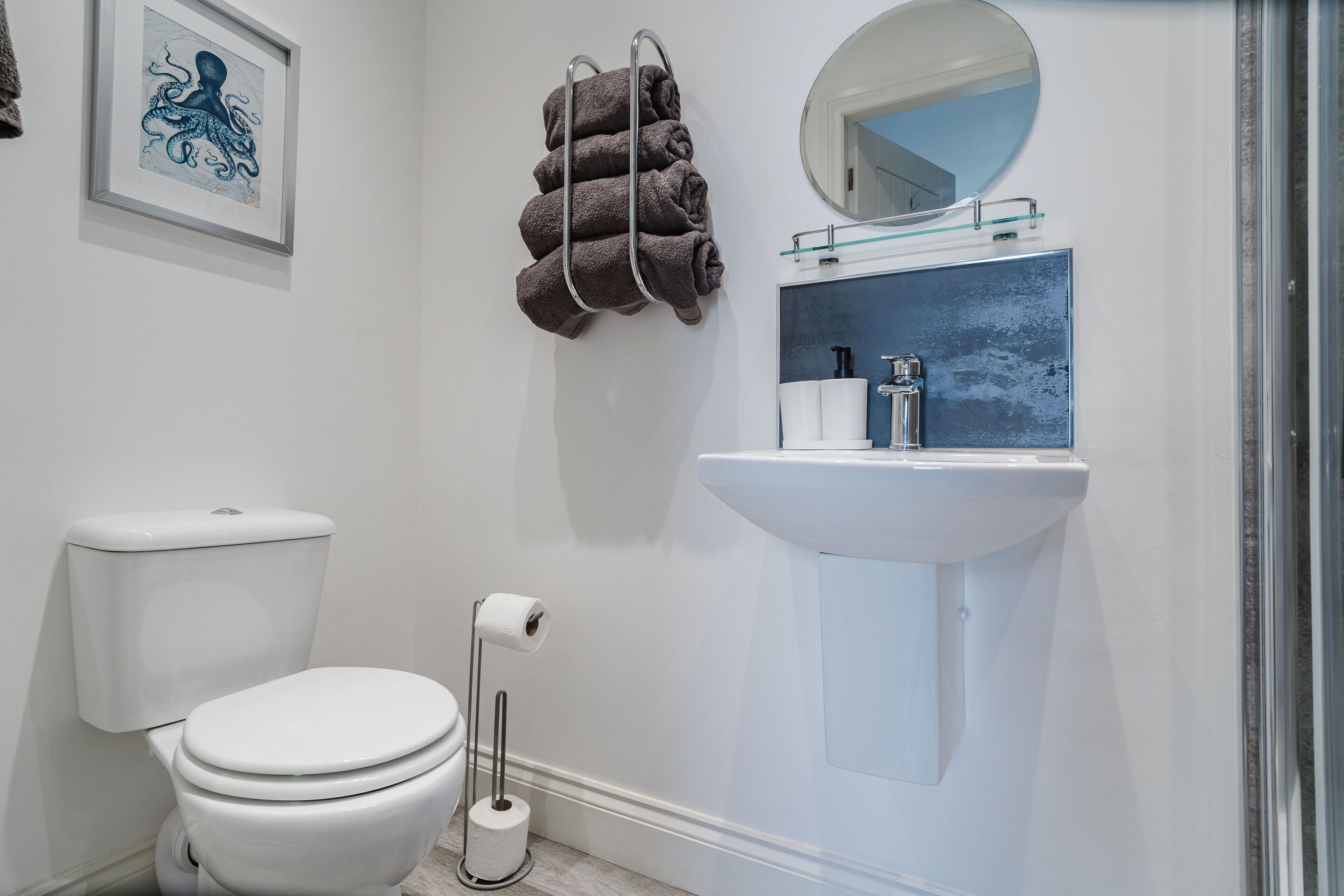 Un baño con inodoro blanco, lavamanos con espejo y una obra de arte enmarcada en la pared.