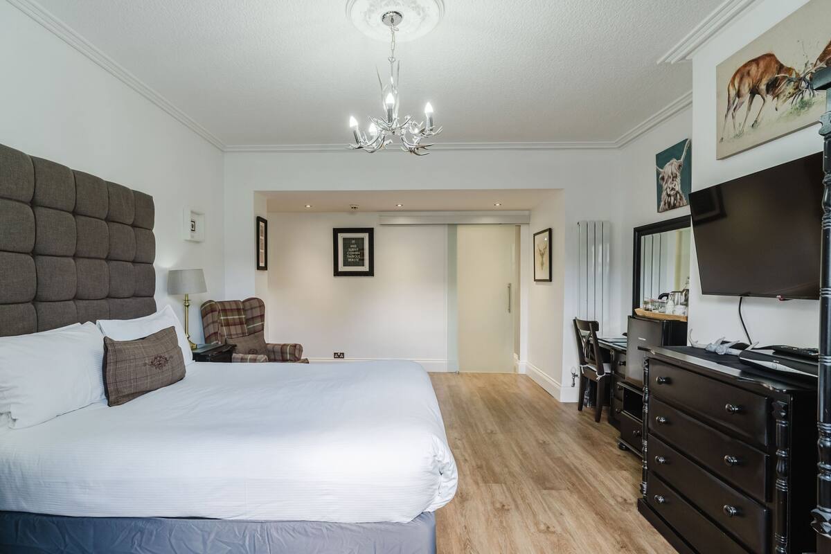 A bedroom with a large bed, a dresser, a television, and a chandelier.