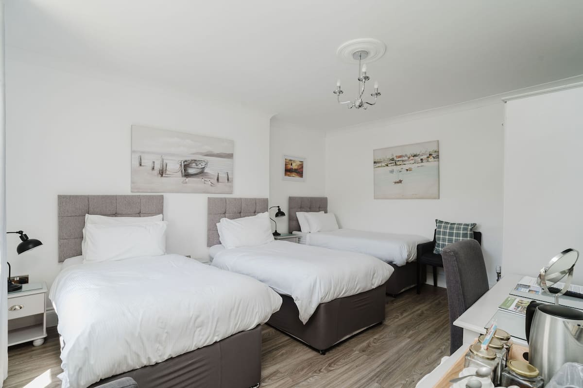 A modern hotel room with two beds, a desk, a chair, a chandelier, and artwork on the walls.