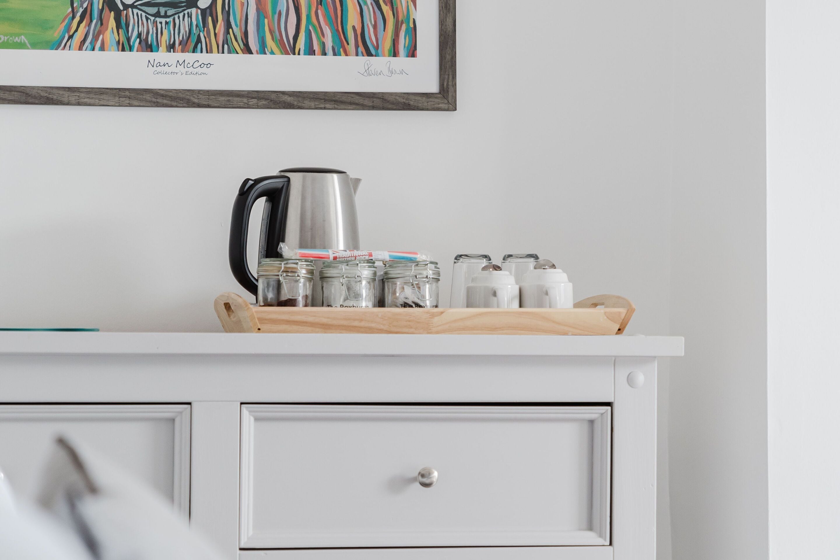A kitchen counter with a coffee maker, jars, and a wooden tray.
