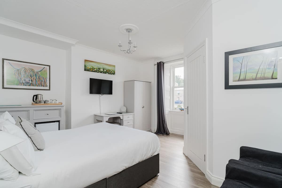 A modern bedroom with a large bed, a desk, a wardrobe, and a TV.