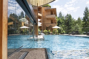 A modern hotel with a swimming pool, outdoor seating, and a view of the surrounding forest.