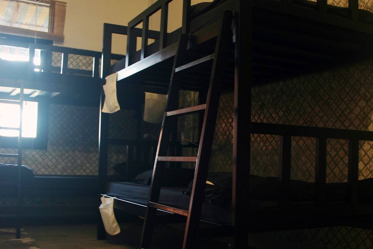 A bunk bed with a ladder, a window with curtains, and a patterned floor.
