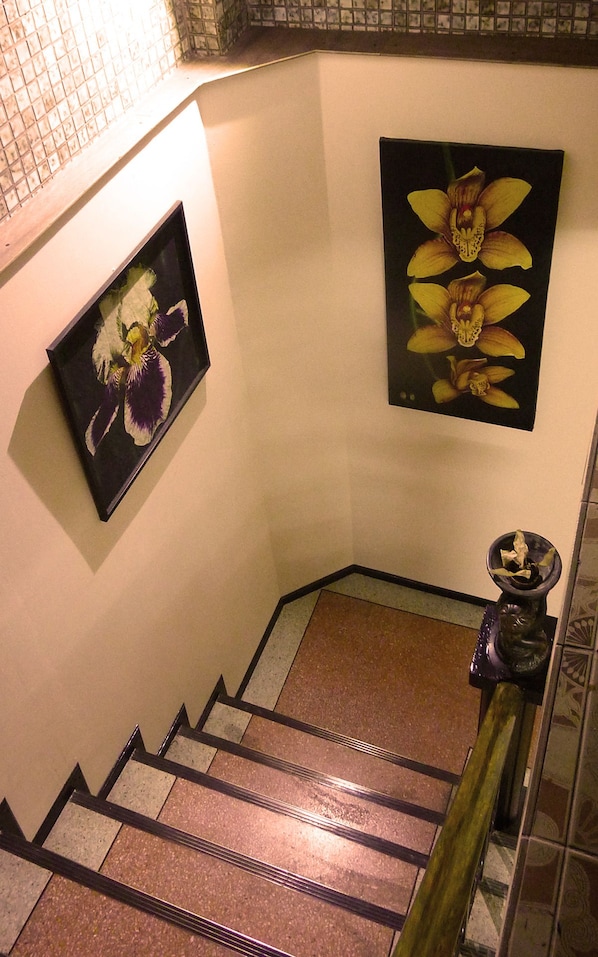A staircase with a handrail, a framed picture of flowers on the wall, and a small potted plant on the landing. - Born Free Hostel (Bangkok)