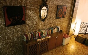A room with a tiled wall, a bookshelf with various books, a mirror, and a small statue on a cabinet. - Born Free Hostel (Bangkok)