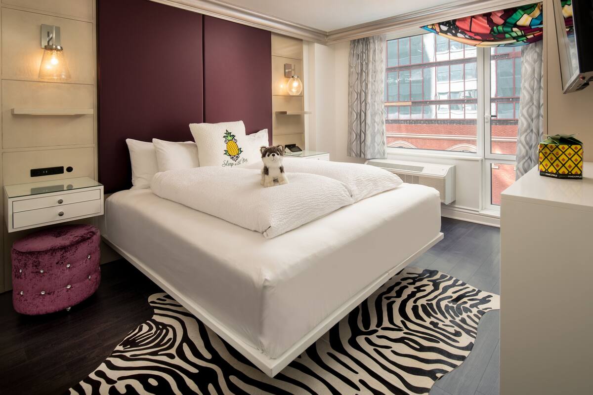 A modern hotel room with a large bed, a zebra-patterned rug, and a view of the city through the window.