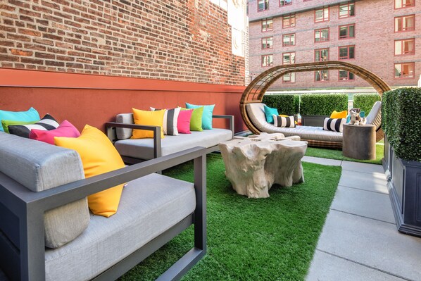 An outdoor seating area with sofas and chairs, a stone table, and a brick wall in the background. - Staypineapple, An Artful Hotel, Midtown (New York)