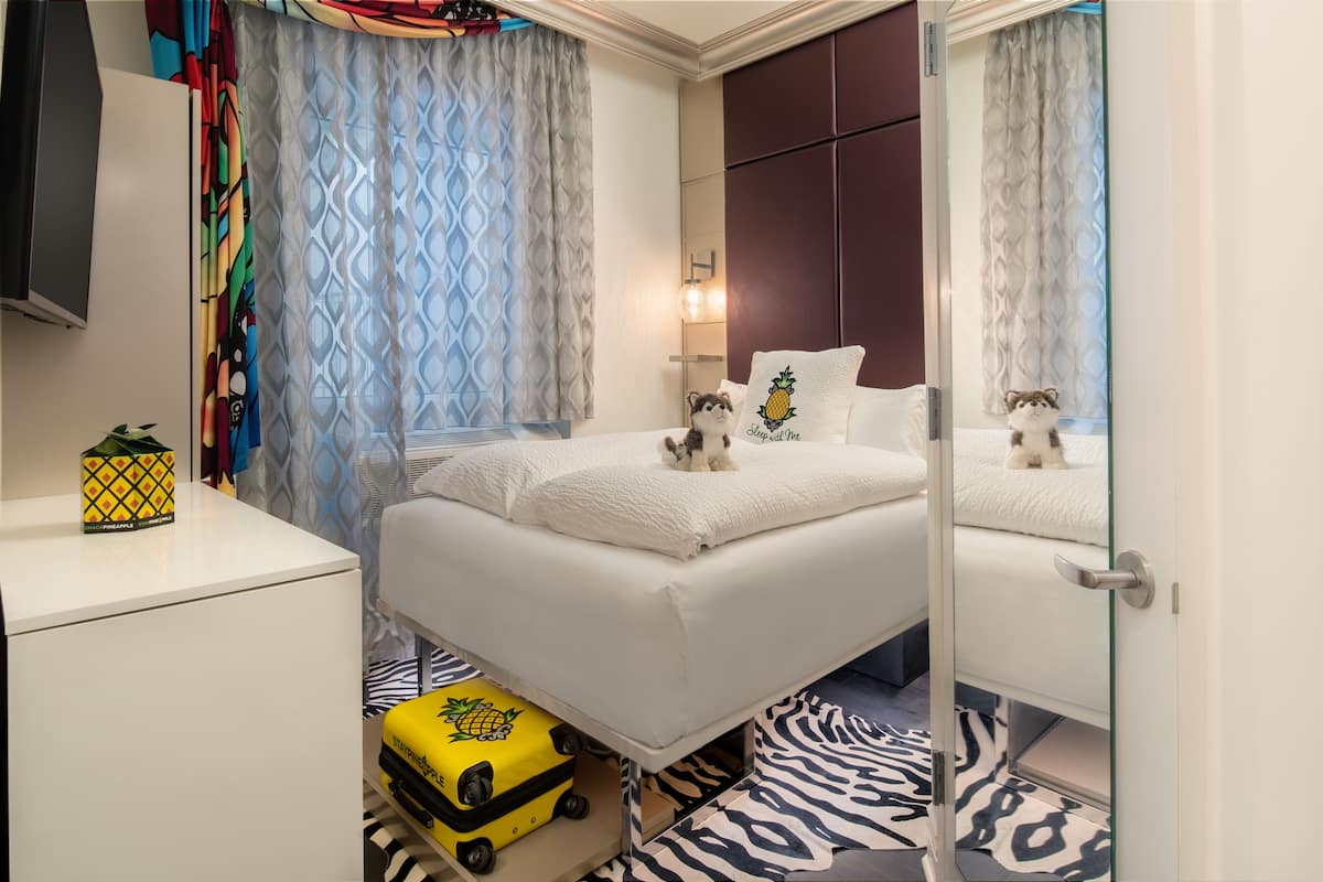 A hotel room with a bed, a small table, a suitcase, and a mirror.