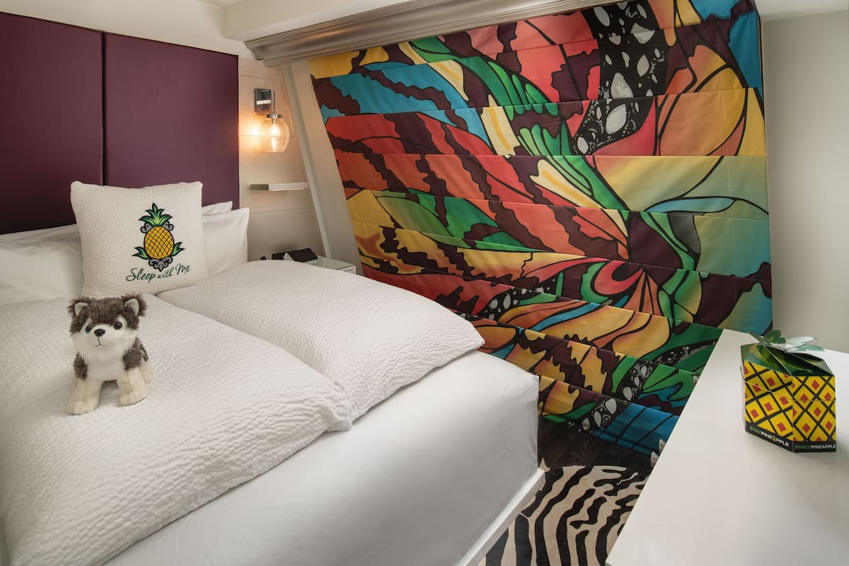 A bed with a plush toy, a pillow with a pineapple design, and a colorful tapestry.