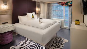 Una habitación de hotel moderna con una cama grande, un reposapiés pequeño y redondo, una alfombra con estampado de cebra y una ventana con cortinas.