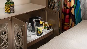 A hotel room with a minibar, a coffee maker, a pineapple-themed mug, and a water bottle.