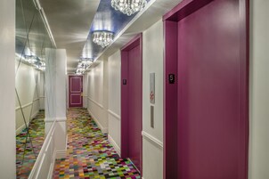 Un pasillo con piso de cuadros coloridos, puertas moradas y candelabros.