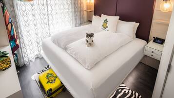 A neatly made bed with a plush toy, a small bedside table with a lamp, and a zebra-patterned rug.