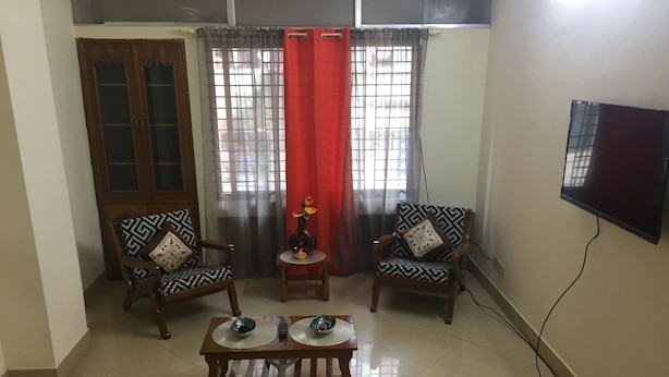 A living room with two patterned armchairs, a coffee table, a TV mounted on the wall, and a wooden cabinet. - Latif villa (Dhaka)