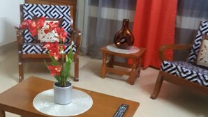 A living room with a wooden coffee table, two patterned chairs, a small side table with a vase, and a red curtain. - Latif villa (Dhaka)
