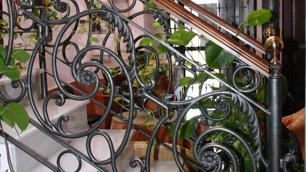 A staircase with ornate black metal railings and a wooden handrail. - Hotel Rural El Olivo (La Puebla de los Infantes)