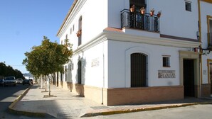 A white building with a balcony, a door labeled "CASA RURAL MEL OLIVO," and a tree in front. - Hotel Rural El Olivo (La Puebla de los Infantes)