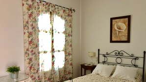 A bedroom with a floral bedspread, a metal bed frame, a bedside table with a lamp, and a framed artwork on the wall. - Hotel Rural El Olivo (La Puebla de los Infantes)