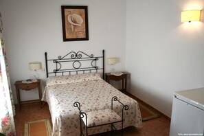 Een slaapkamer met een bed, twee nachtkastjes, een wandlamp en een kunstwerk in een lijst boven het bed.